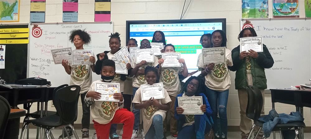 A classs group photo in Kisha Armour-Barber's classroom. All students are holding up their Champs certificates, smiling A classs group photo in Kisha Armour-Barber's classroom. All students are holding up their Champs certificates, smiling